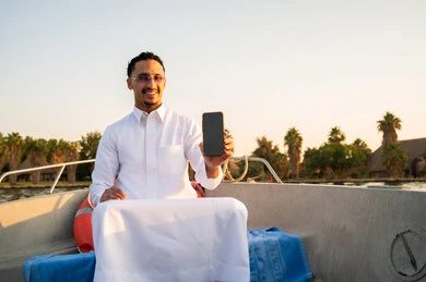 رجل سعودي في قارب يحمل هاتفاً وقت الغروب