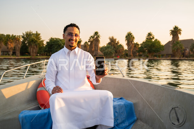 Saudi Man in Thobe on Boat Holding Smartphone