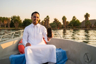 رجل سعودي بالثوب على قارب يحمل هاتف ذكي