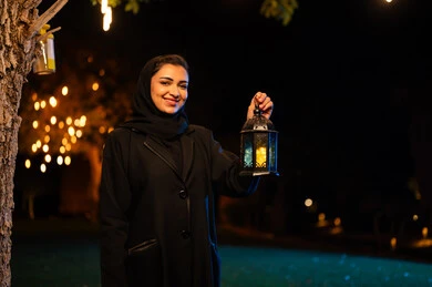 امرأة عربية تحمل فانوساً في حديقة ليلية