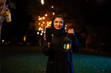 امرأة عربية تحمل هاتف ذكي وفانوس رمضان ليلاً