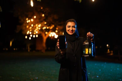 امرأة سعودية تحمل هاتف ذكي وفانوس رمضان ليلاً