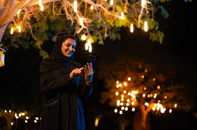 امرأة سعودية تستخدم الهاتف الذكي مع أضواء ليلية