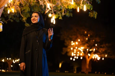 امرأة سعودية مع هاتف ذكي وأضواء أشجار ليلية