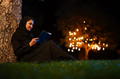 امرأة سعودية تقرأ كتاباً في الحديقة ليلاً