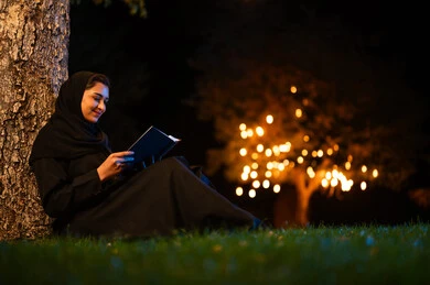امرأة إماراتية تقرأ كتاباً في الهواء الطلق ليلاً