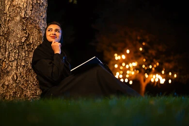 امرأة عربية تقرأ كتاباً في الحديقة ليلاً