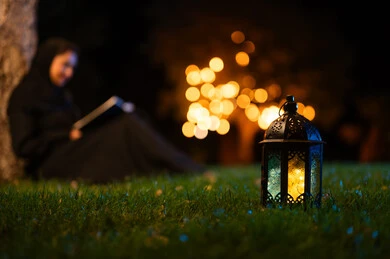 امرأة سعودية تقرأ بجوار فانوس في حديقة ليلية