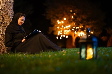 امرأة سعودية تقرأ كتاباً في الحديقة ليلاً مع فانوس