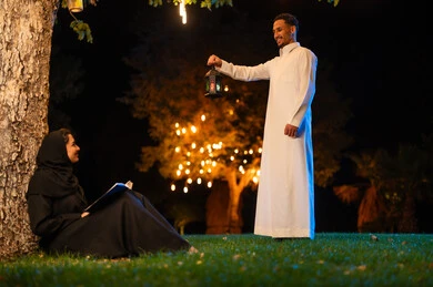 رجل وامرأة سعوديان مع فانوس في حديقة ليلية