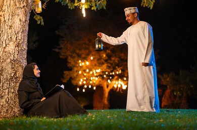 رجل وامرأة بزي عُماني مع فانوس ليلاً في حديقة