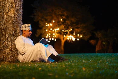Omani Man Reading Book Under Tree at Night