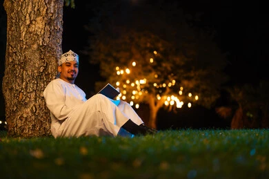رجل عماني بالزي التقليدي يقرأ كتاباً في الحديقة ليلاً