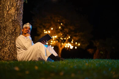 رجل عماني بالزي التقليدي يقرأ في الليل