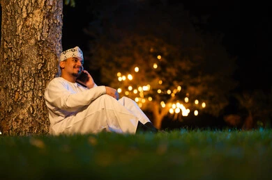 رجل عماني يستخدم الهاتف في حديقة ليلية