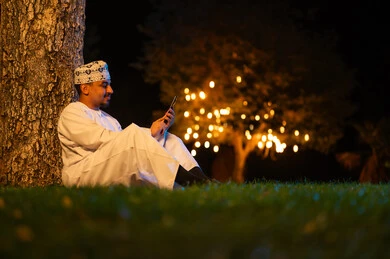 رجل عماني يستخدم الهاتف الذكي في حديقة ليلاً