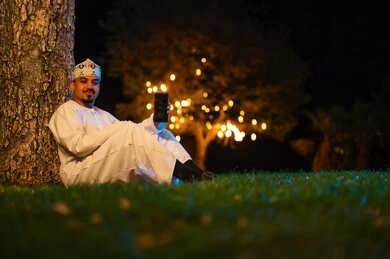 رجل عُماني يحمل هاتف ذكي في حديقة عامة بالليل
