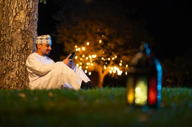 رجل عماني يستخدم الهاتف الذكي في الخارج ليلاً