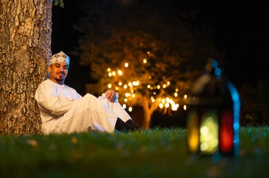 رجل عماني يجلس في حديقة ليلاً مع فانوس