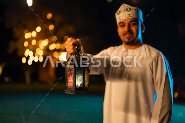 رجل عماني بالزي التقليدي يمسك فانوس رمضان ليلاً