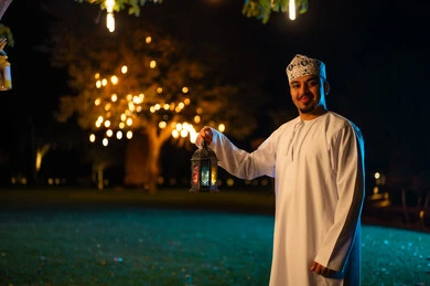 رجل عماني بالزي التقليدي يحمل فانوساً في الليل