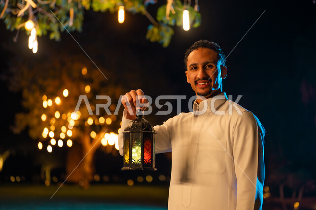 Saudi Man in White Thobe Holding Lit Lantern at Night