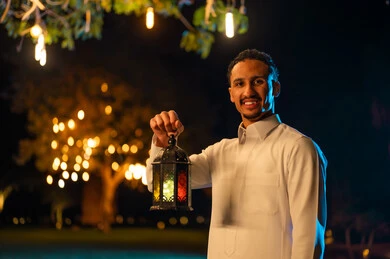 Saudi Man in White Thobe Holding Lit Lantern at Night
