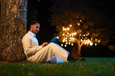 Saudi Man in Thobe Reading Book at Night