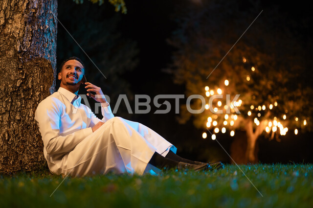 Saudi Man in Thobe Using Smartphone in Night Park