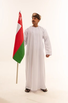 رجل عماني بالزي التقليدي يحمل علم سلطنة عمان