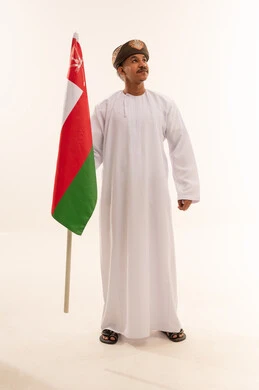 رجل عماني بالزي التقليدي يحمل علم سلطنة عمان