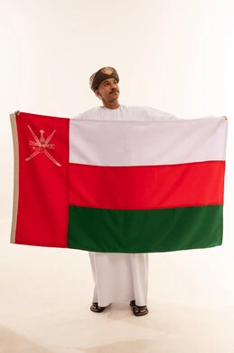 رجل عماني بالزي التقليدي يحمل علم سلطنة عمان