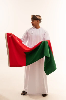 رجل عماني بالزي التقليدي يحمل علم سلطنة عمان