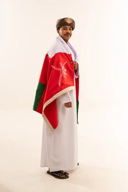 رجل عماني يرتدي علم سلطنة عمان بخلفية بيضاء
