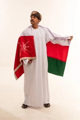 رجل عماني بالزي التقليدي يحمل علم سلطنة عمان