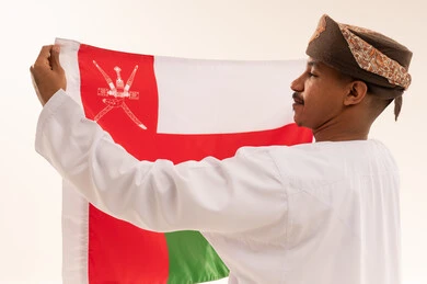 رجل عماني بالزي التقليدي يحمل علم سلطنة عمان