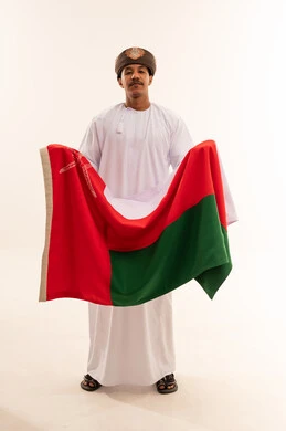 رجل عماني بالزي التقليدي يحمل علم سلطنة عمان