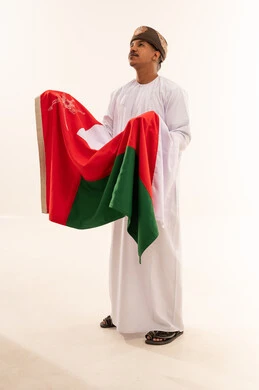 رجل عماني بالزي التقليدي يحمل علم سلطنة عمان