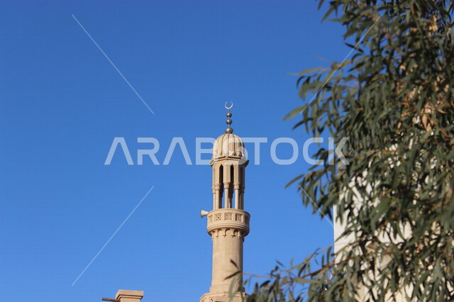 صورة مقربة لمئذنة إحدى المساجد بالمملكة العربية السعودية، العبادة والتقرب إلى الله، صوت الأذان، دعوة المسملين للصلاة، مئذنة المسجد ، منارة المسجد، اغصان الشجر