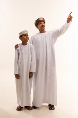 رجل وصبي عُماني بالزي التقليدي يشيران للأعلى بخلفية بيضاء