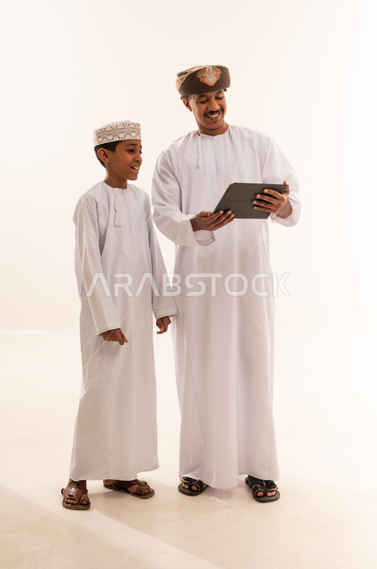 رجل وطفل عمانيان يستخدمان جهازاً لوحياً في الاستوديو