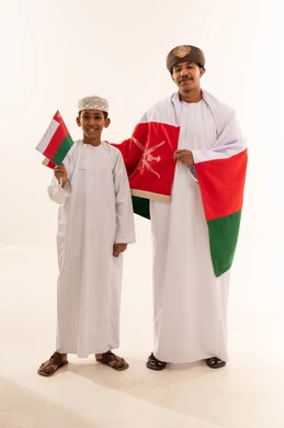 رجل وطفل عماني بالزي التقليدي مع علم عمان