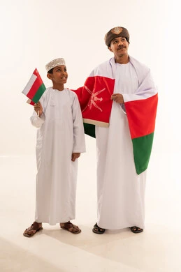رجل وطفل عماني بالزي التقليدي مع العلم الوطني