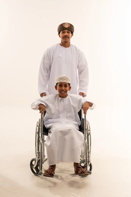 رجل وصبي عماني على كرسي متحرك بخلفية بيضاء