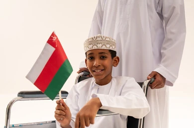 طفل عماني على كرسي متحرك يحمل علم عمان