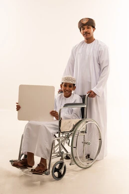 رجل وطفل عماني على كرسي متحرك مع لوحة فارغة
