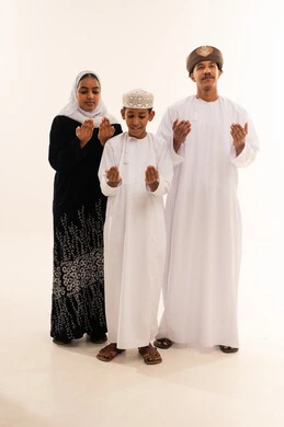 عائلة عمانية بالزي التقليدي تدعو أمام خلفية بيضاء