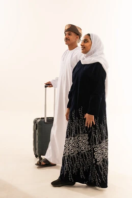 زوجان عمانيان مع حقيبة سفر على خلفية بيضاء