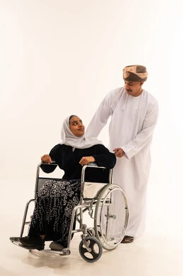 رجل عُماني يساعد امرأة على كرسي متحرك خلفية بيضاء