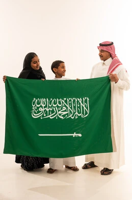 عائلة سعودية تحمل العلم الوطني بالزي التقليدي